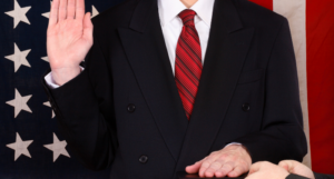 a photo of a white man in a suit getting sworn in on a book with an American flag in the background